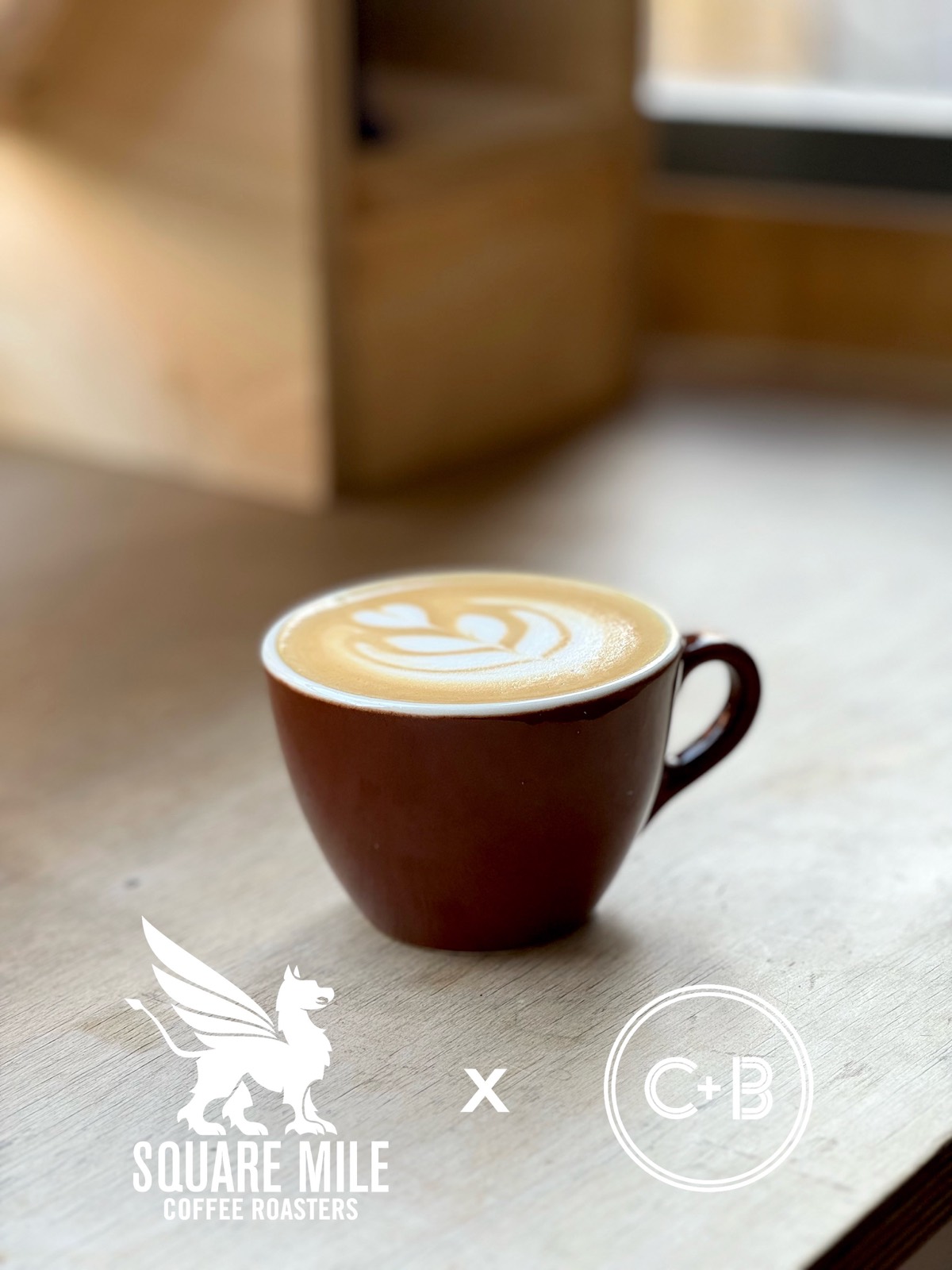 A flat white in a brown Square Mile cup on the Coffee + Beer windowsill, with the Square Mile and C+B logos